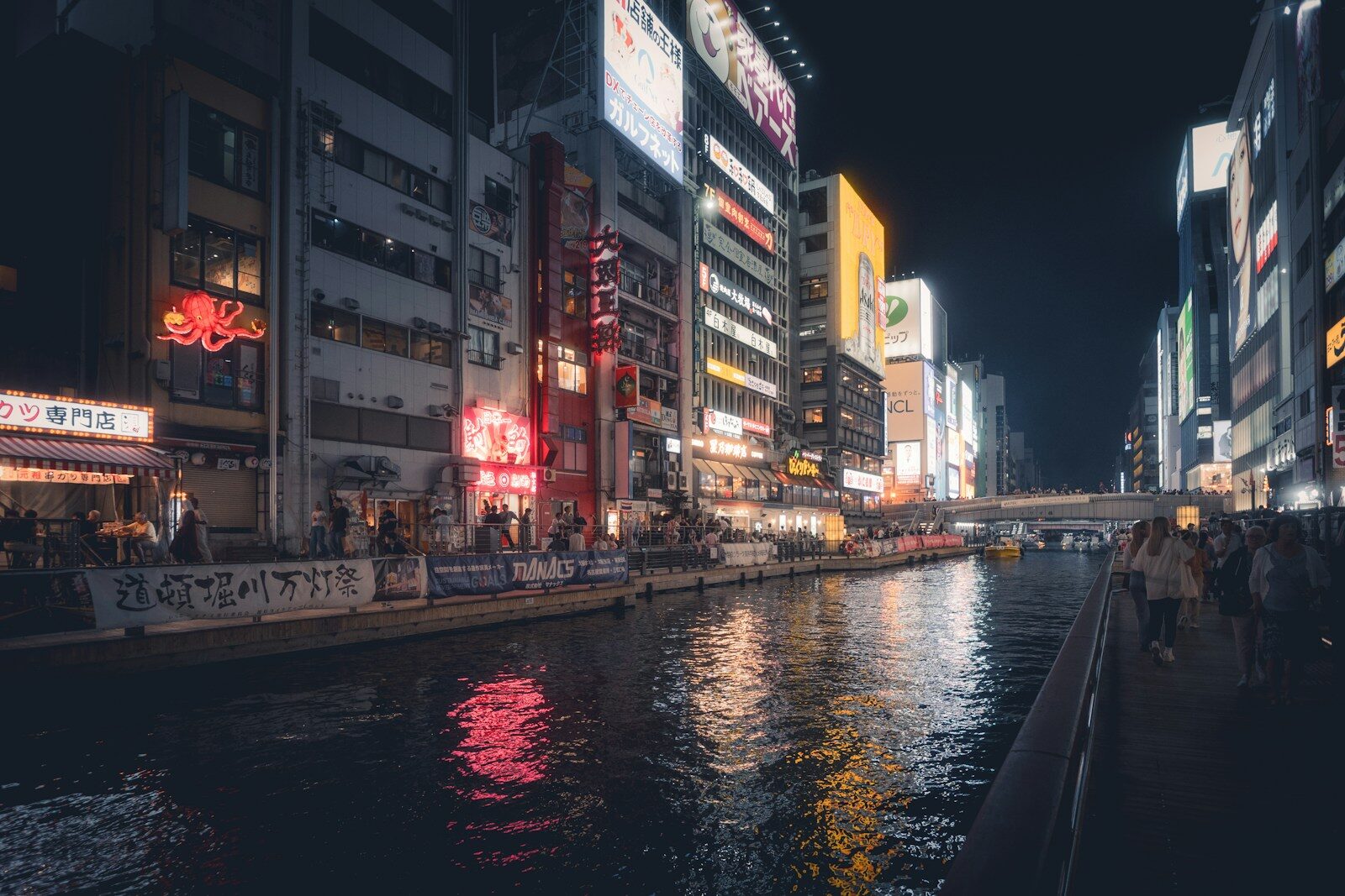 Cityscape at night with glowing signs reflecting in water.
